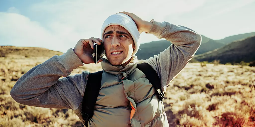 A disoriented man using his cellphone in a sunlit desert 