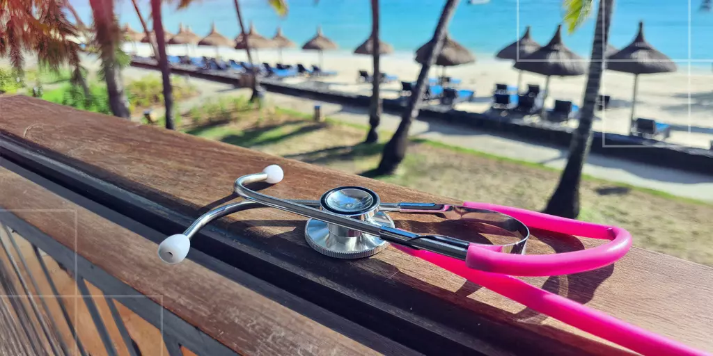 Stéthoscope rose posé sur une rambarde en bois, avec vue sur une plage tropicale et des chaises longues sous des parasols de paille.